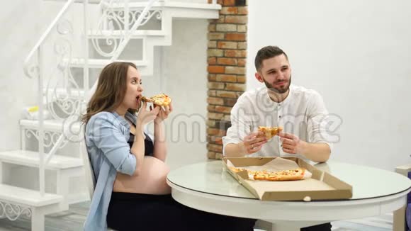 男人和孕妇在家里厨房里吃披萨一顿高脂肪的饭饿了视频的预览图