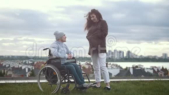 坐在轮椅上的残疾男子和在山上说话的女人视频的预览图