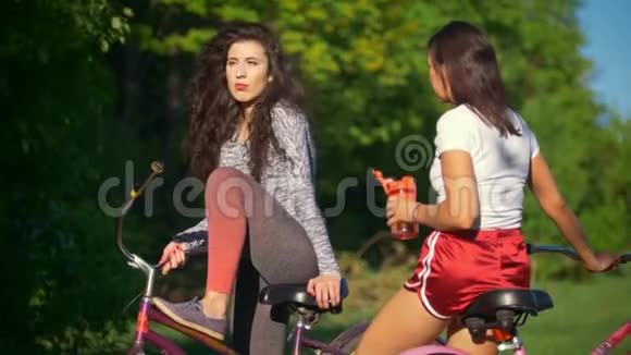 骑自行车休息两个女骑自行车的人喝水和交谈阳光明媚的夏日视频的预览图