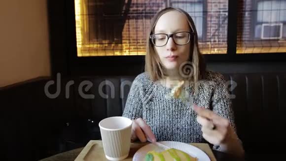 戴眼镜的时髦女孩切下一小块朋克蛋糕蘸上甜果糖浆喝热浆果茶视频的预览图