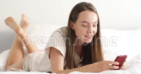 微笑的女人在床上使用智能手机视频的预览图