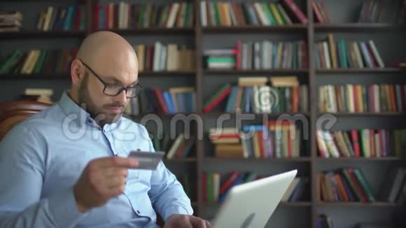 男人用信用卡在线购物年轻人在网上使用信用卡他的笔记本电脑在家里的背景下视频的预览图