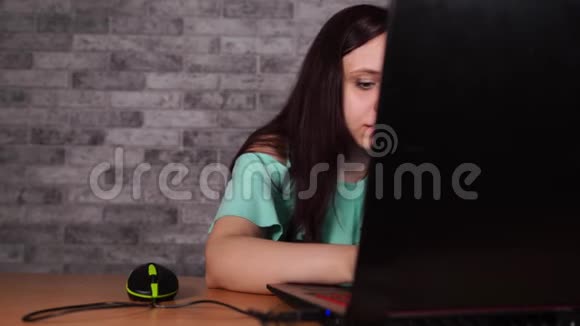 年轻女子看着笔记本电脑的显示器集中深色上衣裸肩浏览同时工作视频的预览图