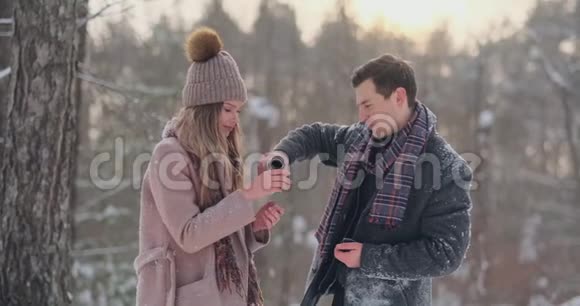 情侣在冬天的森林里喝热水瓶里的茶冬天公园里穿外套的时髦男女视频的预览图