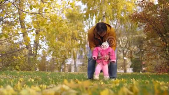 婴儿和他的父亲跳着脚在绿色的草地上秋天和微笑慢动作视频的预览图
