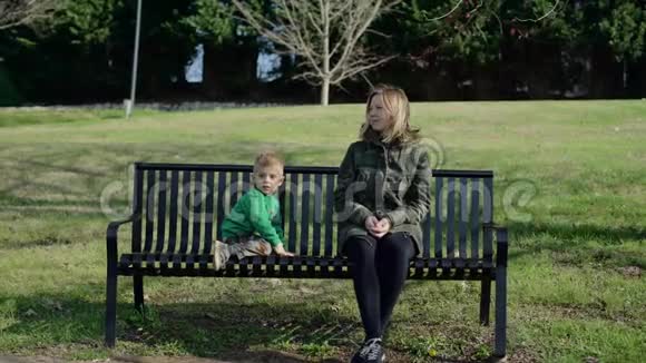 美丽的年轻母亲和儿子坐在公园的长凳上视频的预览图