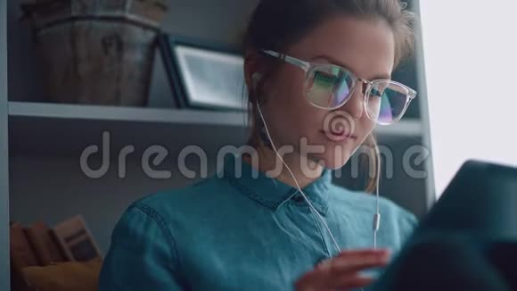 时髦的学生女孩坐在窗边读一本电子书视频的预览图