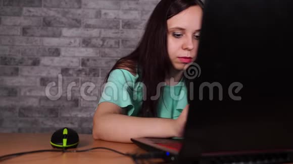 年轻女子看着笔记本电脑的显示器集中深色上衣裸肩浏览同时工作视频的预览图