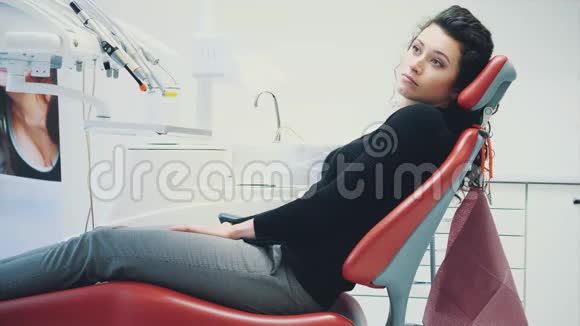 在牙科诊所接待牙医的女人她坐在一张红椅子上害怕一个病人看着视频的预览图