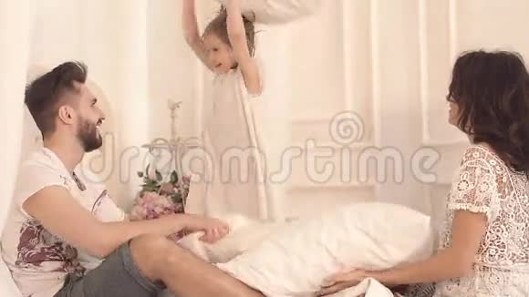 幸福的三口之家母亲父亲和女儿在床上打枕头仗视频的预览图