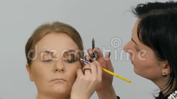 专业主妆师将米色眼影在美容院闭眼处用特殊刷子刷上模型眼视频的预览图