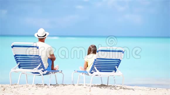父亲和女儿在热带海滩上坐在躺椅上欣赏着大西洋的景色视频的预览图