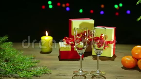 圣诞树旁边的香槟酒杯燃烧的蜡烛和礼物放在黑色背景的木桌上视频的预览图
