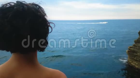 卷发的女人站在悬崖上在海上看白色的游艇视频的预览图