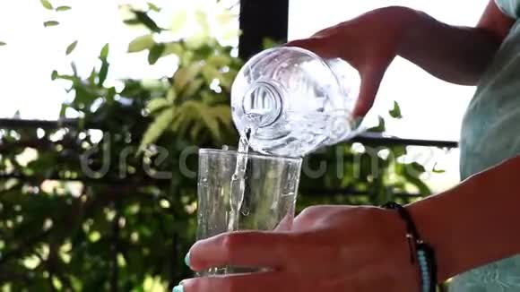 灌一杯清水靠近一个女人在阳台上从一个瓶子向一个玻璃杯倒水视频的预览图