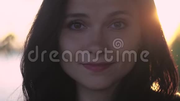 在湖边日落背景下一位年轻漂亮的黑发女人的特写肖像视频的预览图