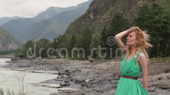 年轻的女人穿着一件长长的流动的衣服在河山的背景上穿绿色衣服的女人视频的预览图