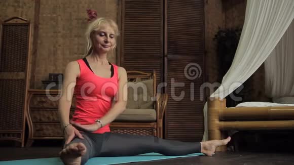 老年女性金发女郎正坐在房间里的佛像上伸展肌肉视频的预览图