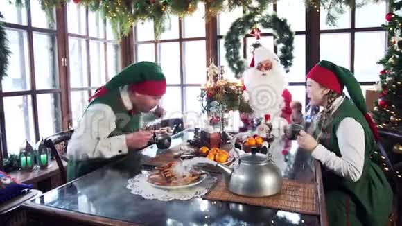 饥饿的精灵和圣诞老人在节日的餐桌上吃饭视频的预览图