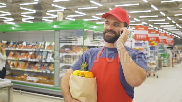一个英俊的送货员带着购物袋在超市里用智能手机点餐视频的预览图