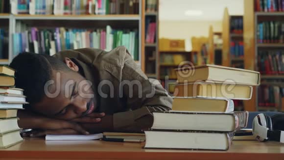 非裔美国人英俊的年轻男学生正坐在桌子旁图书馆里有一大堆书他的头在躺着视频的预览图
