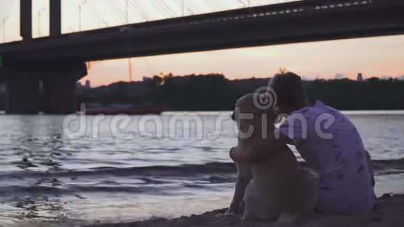 年轻人正和一只狗坐在河岸上视频的预览图