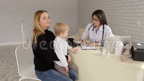 女医生和一个小男孩的母亲交谈并在笔记本上做笔记视频的预览图