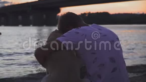 年轻人正和一只狗坐在河岸上视频的预览图
