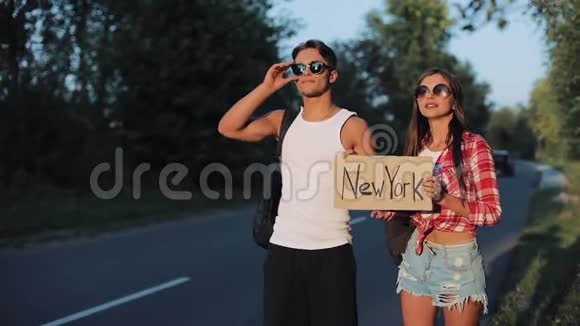 一对年轻夫妇正站在路上搭便车一男一女在高速公路上用纽约的标志停车视频的预览图
