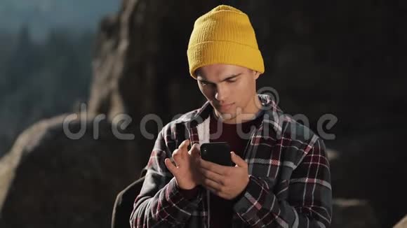 年轻的快乐男人和一个人在美丽的山前站在岩石的顶端的电话聊天通信视频的预览图