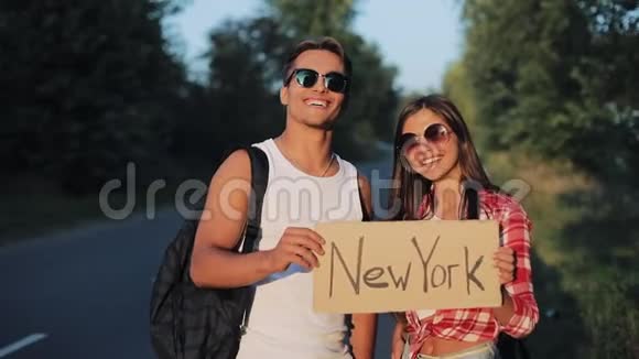 一对年轻夫妇正站在路上搭便车一男一女在高速公路上用纽约的标志停车视频的预览图