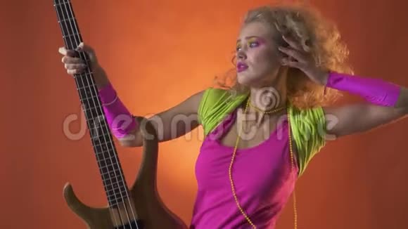 金发的80年代迪斯科舞者用吉他摆姿势橙色背景视频的预览图
