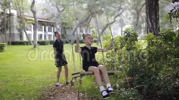 姐姐在阳光下的树下摇着女儿女孩笑高兴公园里的家庭乐趣视频的预览图