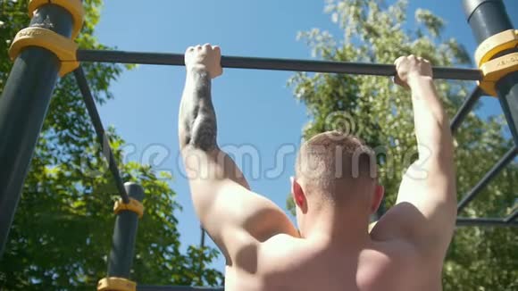 在阳光明媚的一天肌肉发达的人在户外的水平杆上被拉起来的后视图视频的预览图