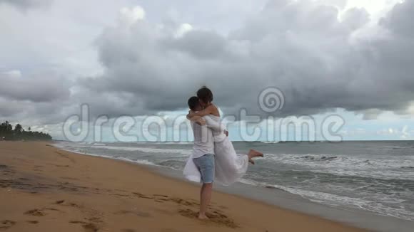 年轻一对相爱的情侣在日落时分在海边旋转拥抱视频的预览图