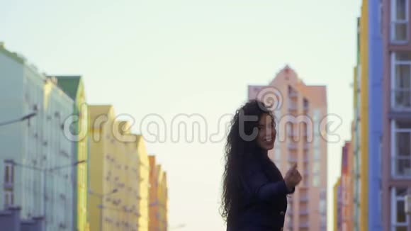 美丽的黑发女郎手持相机挥手邀请她在街上散步视频的预览图