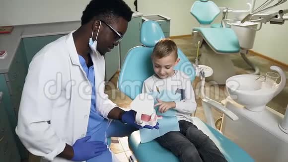 非洲牙医向小男性病人展示塑料牙齿模型视频的预览图