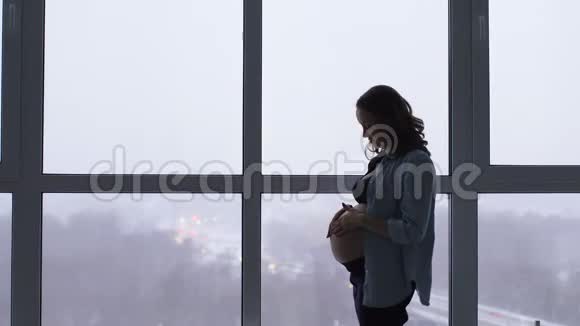 清晨幸福微笑的孕妇在别致的公寓与全景窗户视频的预览图
