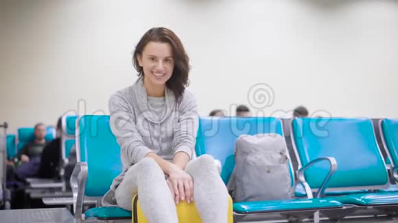 开朗的黑发女孩坐在机场的包上等待她的航班享受她未来的假期和旅行视频的预览图