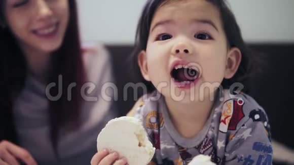 一个可爱的可爱的亚洲幼儿男孩正在他的年轻妈妈旁边吃饼干他的头发是红色的视频的预览图