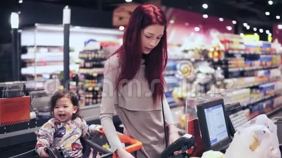 一位红头发的年轻女子正在收银台付钱买东西而她的儿子正笑着坐在购物中心视频的预览图