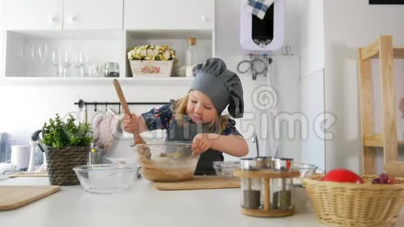 学前女孩面包师用一个大木勺在碗里揉面团视频的预览图