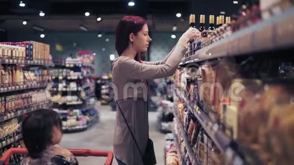 年轻漂亮的女顾客正在当地的超市里挑选香料她蹒跚学步的儿子耐心地等待着她视频的预览图