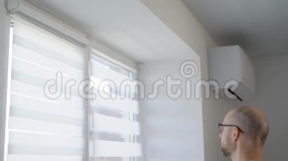 成年男子白天在客厅的窗框上安装百叶窗杆并固定窗帘视频的预览图