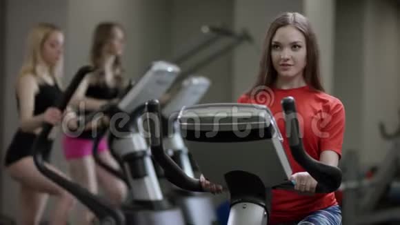 穿红色衬衫的漂亮女孩在运动自行车上大力工作只是在新的健身房里工作视频的预览图