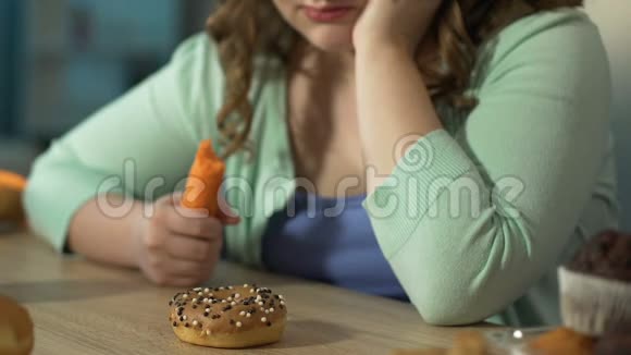 胖女孩一边吃新鲜胡萝卜一边伤心地看着桌上的甜甜圈视频的预览图