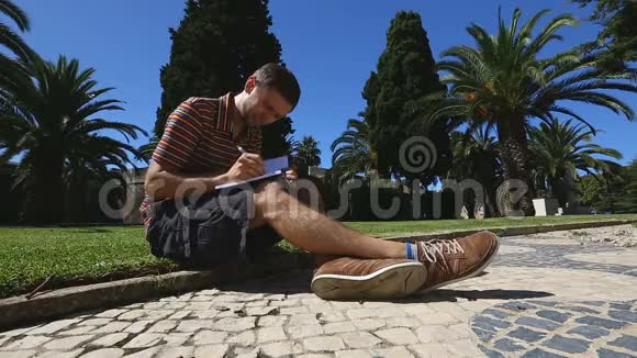 年轻人坐在草坪上写笔记本学生做笔记教育视频的预览图