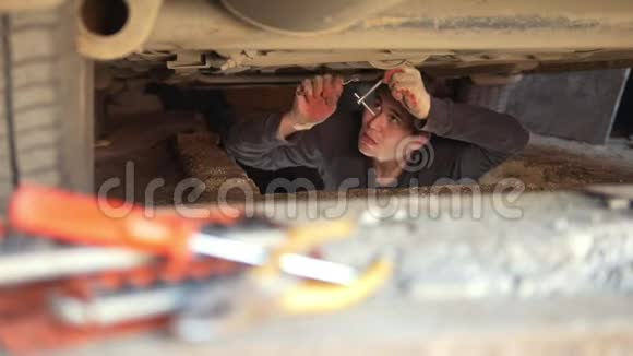 汽车下面的男机修工在车库里修理他的车视频的预览图
