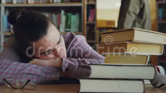 一个英俊的少年正坐在桌上睡在学校图书馆里图书馆里挤满了成堆的人视频的预览图