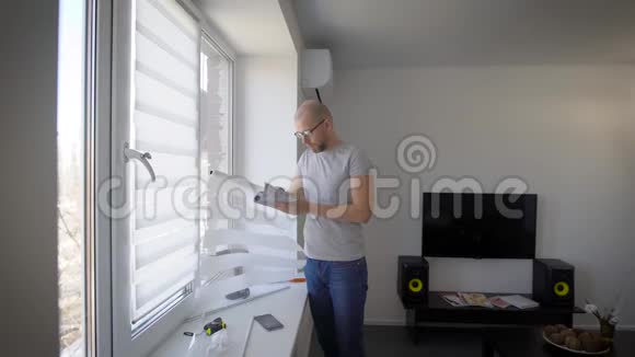 男人正在阅读窗户上窗帘的安装说明站在客厅里看细节视频的预览图